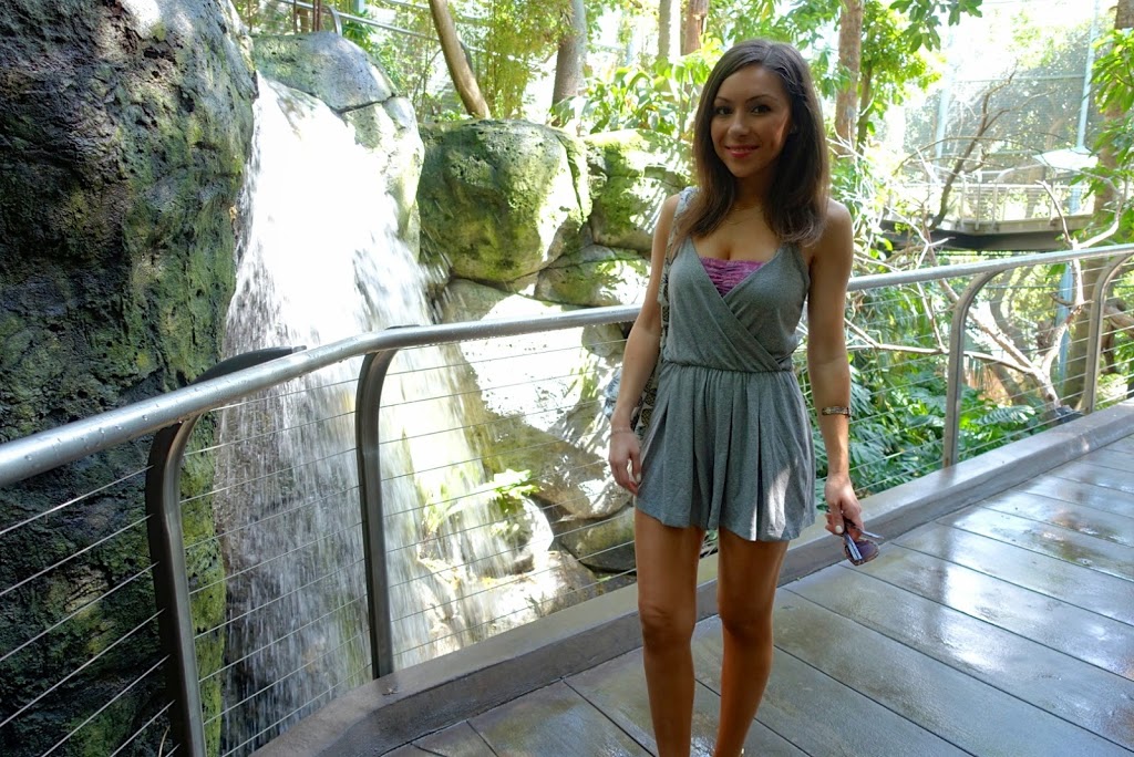 Blogger Nihan posing and showing her outfit, a casual grey romper and a pineapple backpack in the Scripps Aviary at the San Diego Zoo