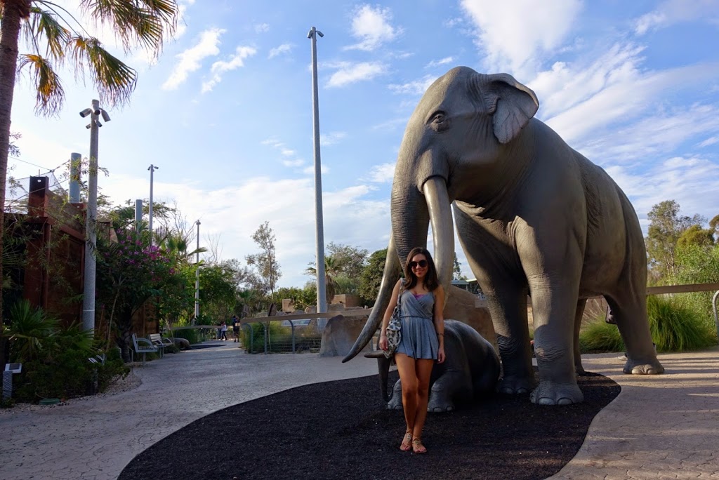 Blogger Nihan posing and showing her outfit, a casual grey romper and a pineapple backpack by the Elephant Sculpture at the San Diego Zoo