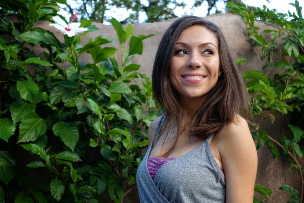 Portrait photo of Blogger Nihan smiling genuinely and showing her outfit, a casual grey romper, on the flower walk at the San Diego Zoo