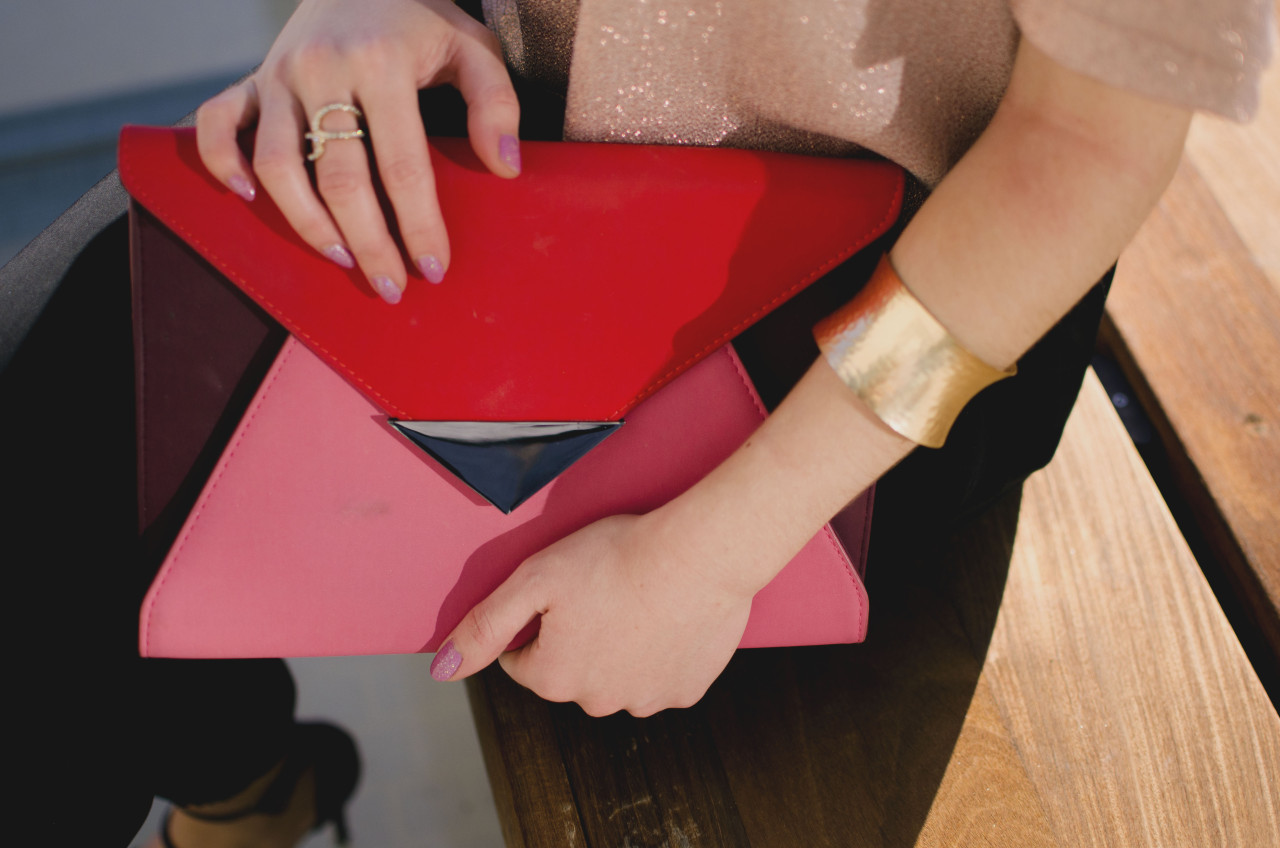 Blogger Nihan showing her rings, pink glittery nails and pink and red color block festive clutch