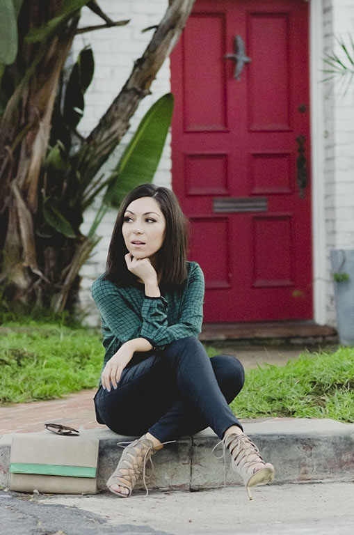 Blogger Nihan sitting in front of a red fancy door, showing her outfit