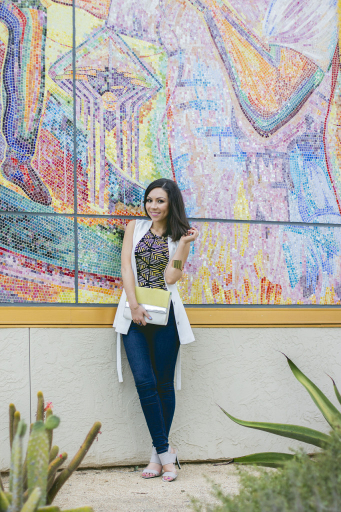 Style with Nihan posing in front of a mural wearing a Topshop white sleeveless jacket, Topshop printed top, dark wash high-waisted jeans and nude high-heels from Forever21